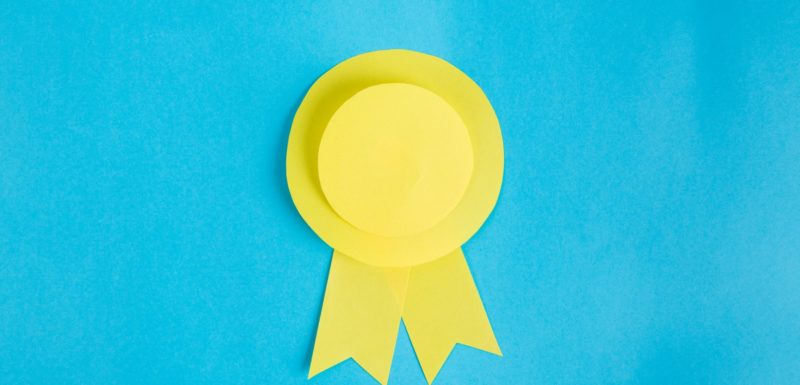 Image of a gold award ribbon with blue background.